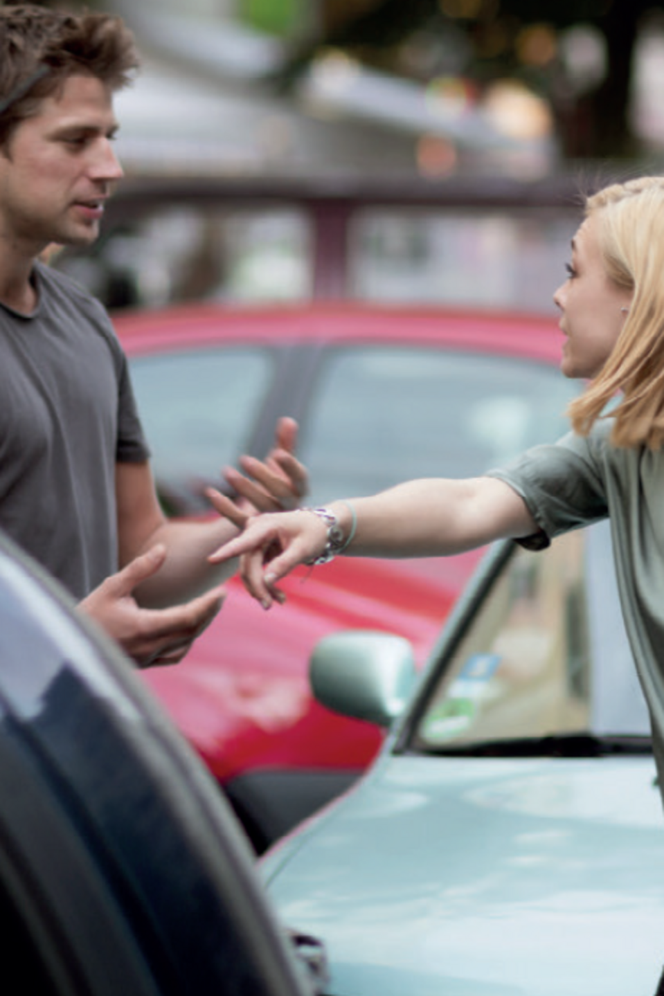 Aggression im Verkehr Ein Mann und eine Frau streiten zwischen zwei Autos auf der Fahrbahn.