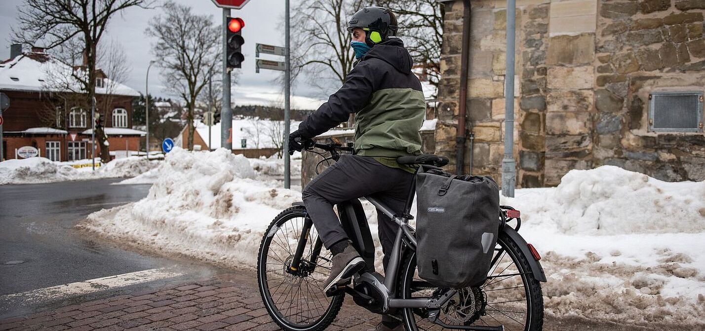 Im Winter an der Ampel. Ein Mann steht mit Fahrrad an einer Ampel in winterlicher Stadtlandschaft.